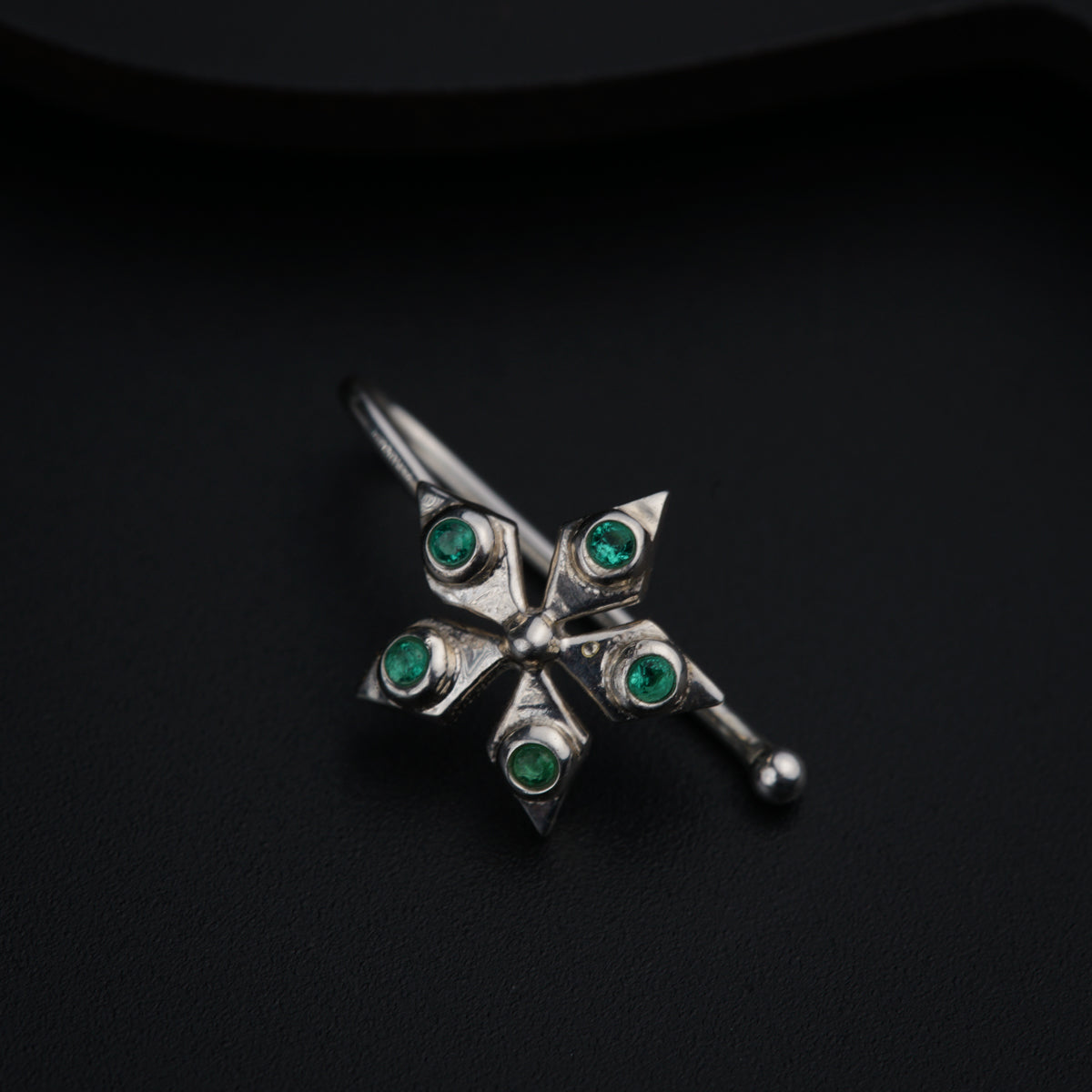 a silver brooch with green stones on a black surface