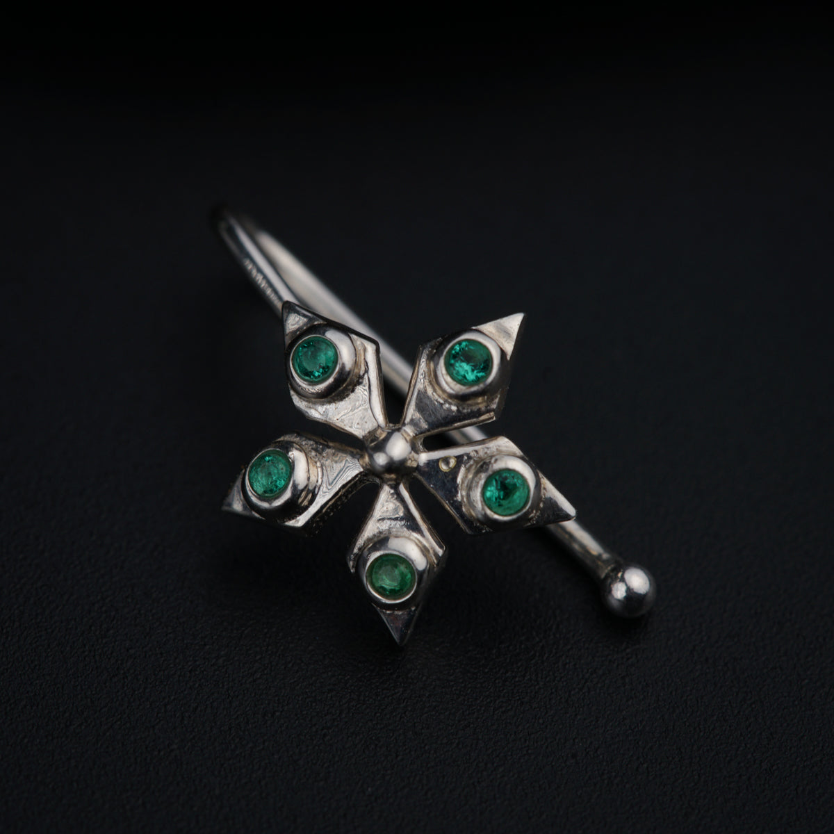 a silver brooch with green stones on a black background