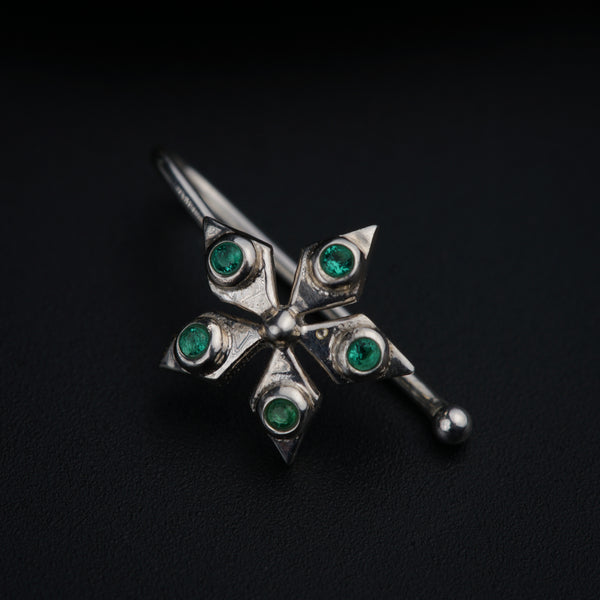 a silver brooch with green stones on a black background