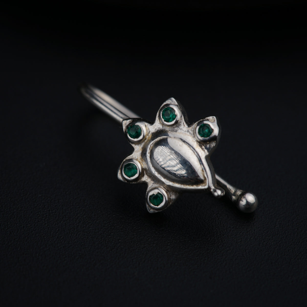 a silver brooch with green stones on a black background