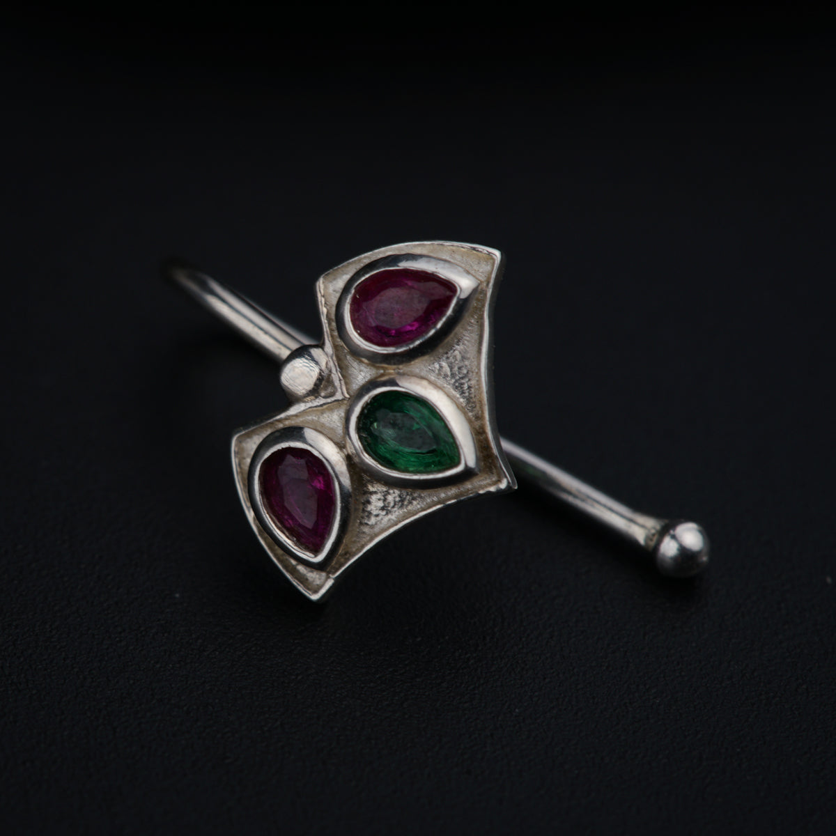 a close up of a silver brooch with a green and red stone