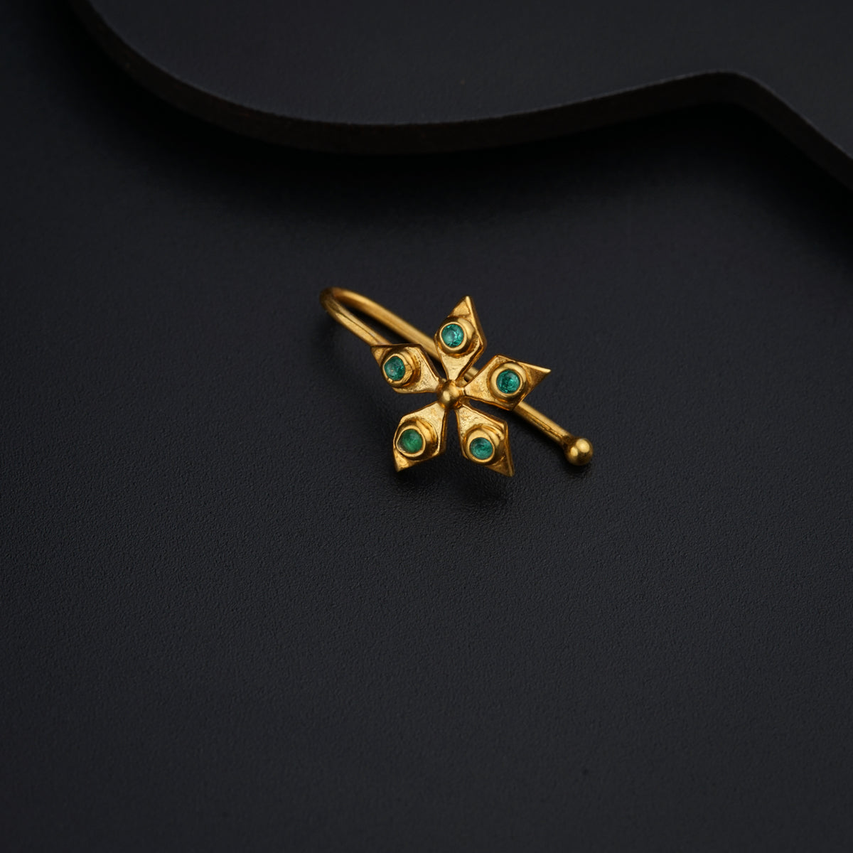 a gold brooch with green stones on a black background