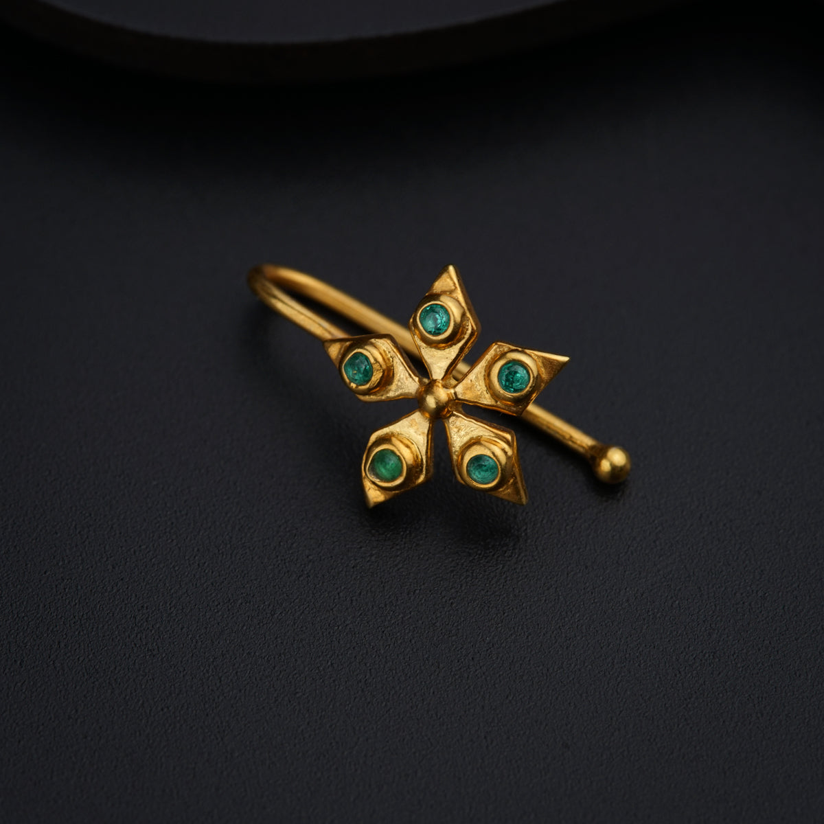 a gold ring with green stones on a black surface