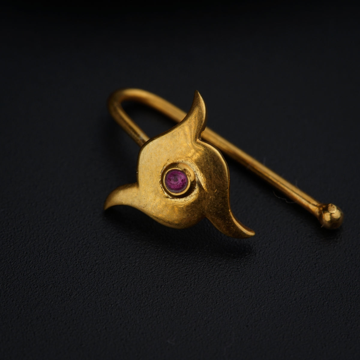 a close up of a gold brooch with a red stone