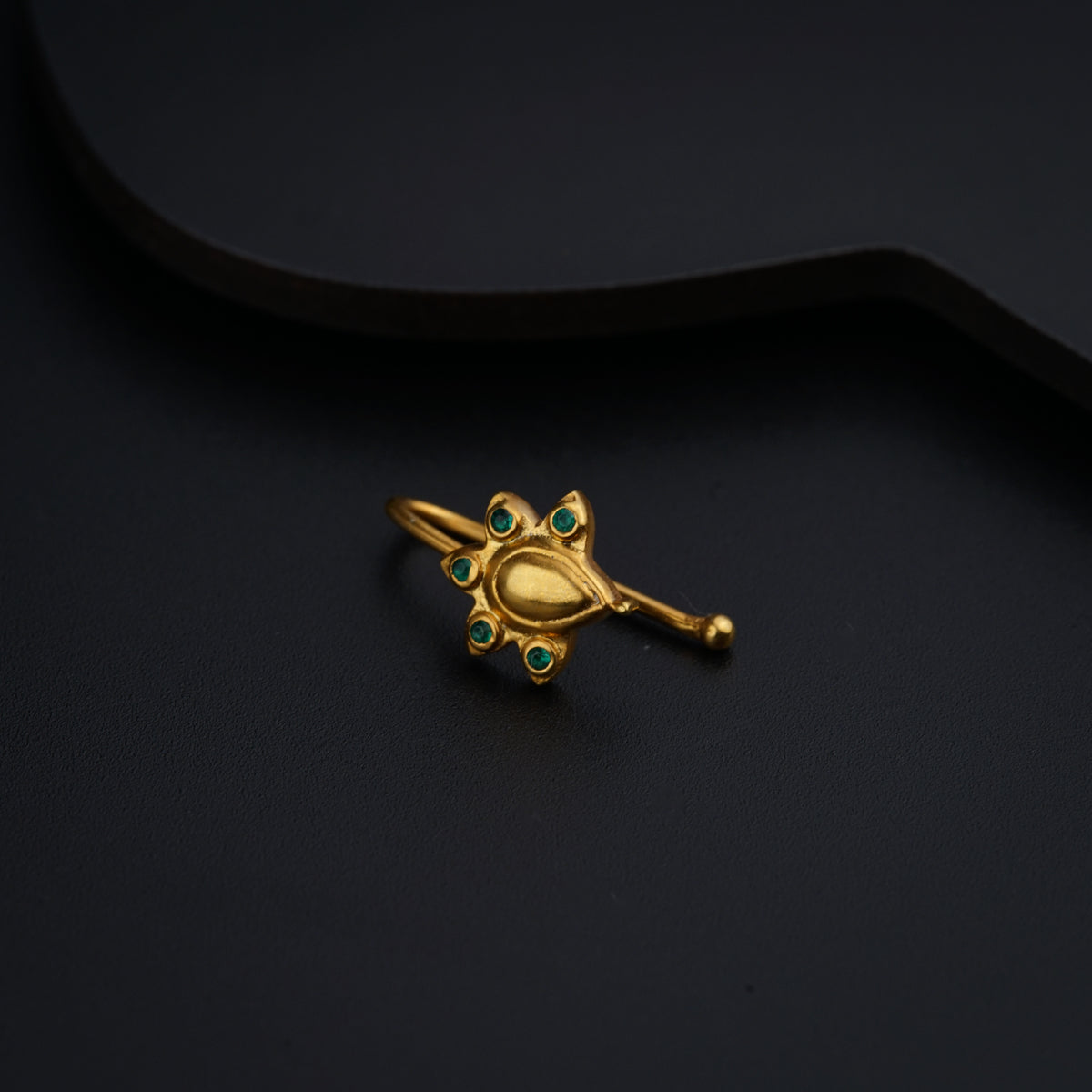 a gold brooch with green stones on a black background