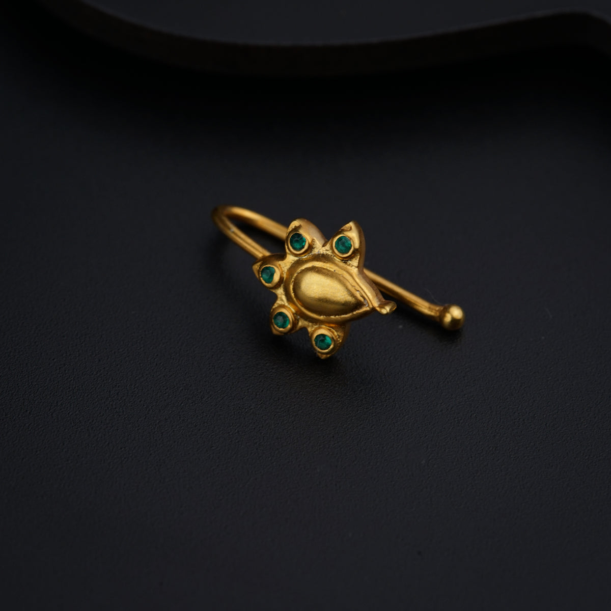 a gold ring with green stones on a black surface
