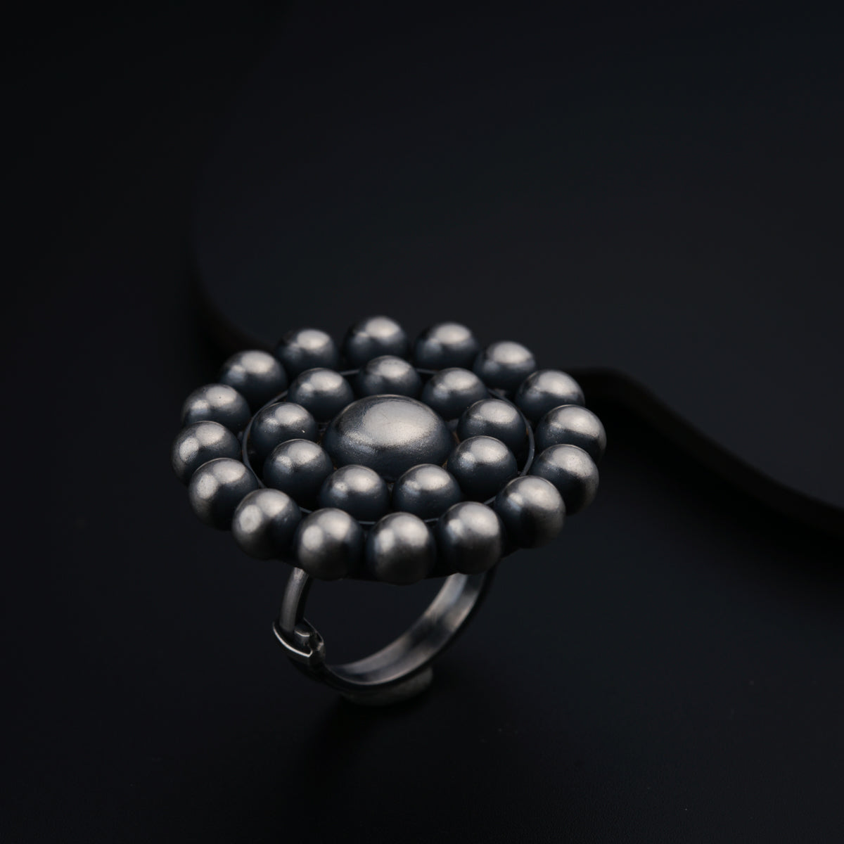 a silver ring with balls on it on a black surface