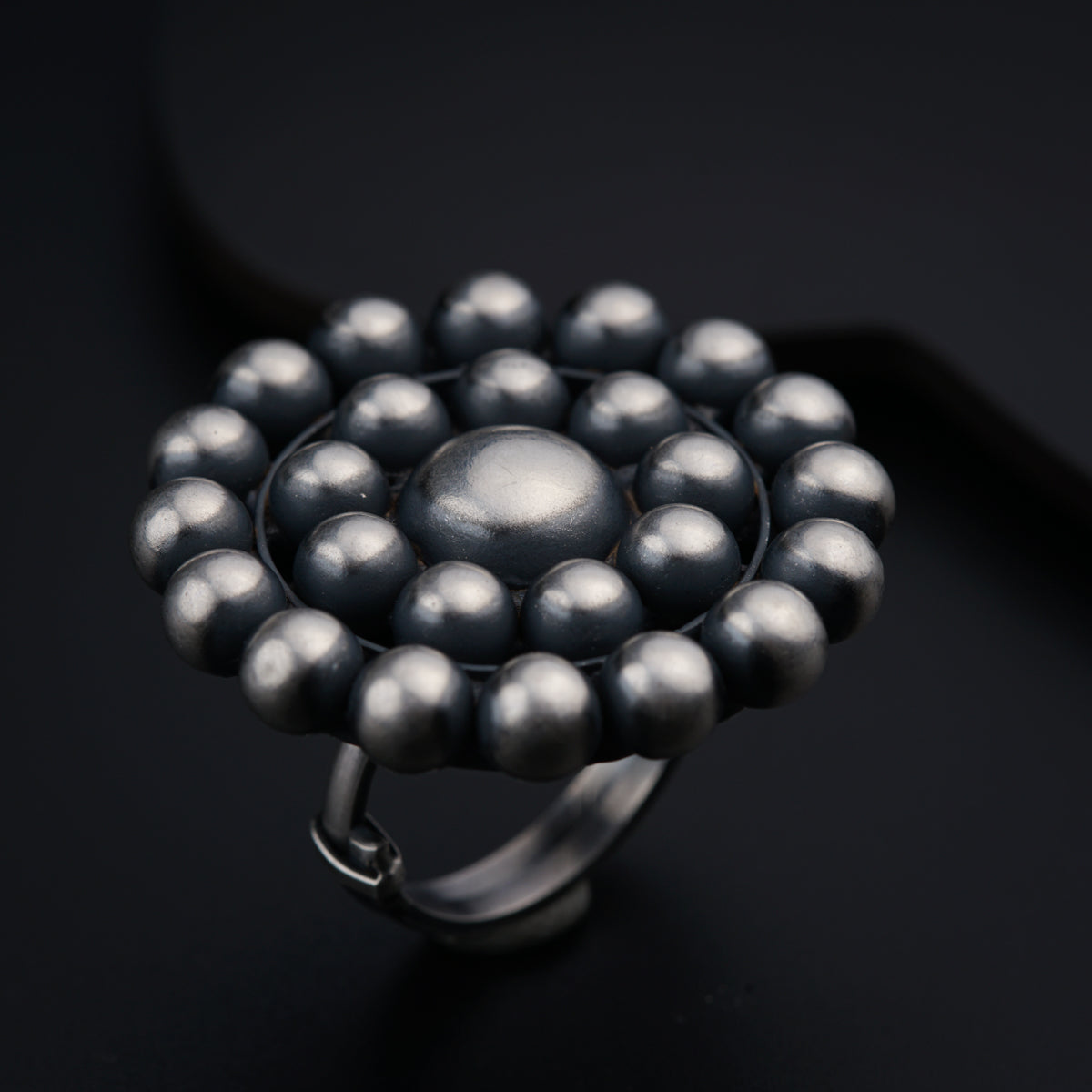 a silver ring with black beads on a black surface
