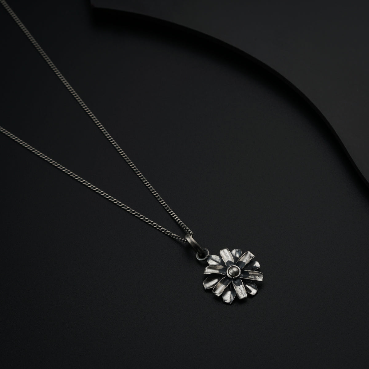 a silver necklace with a flower on a black background