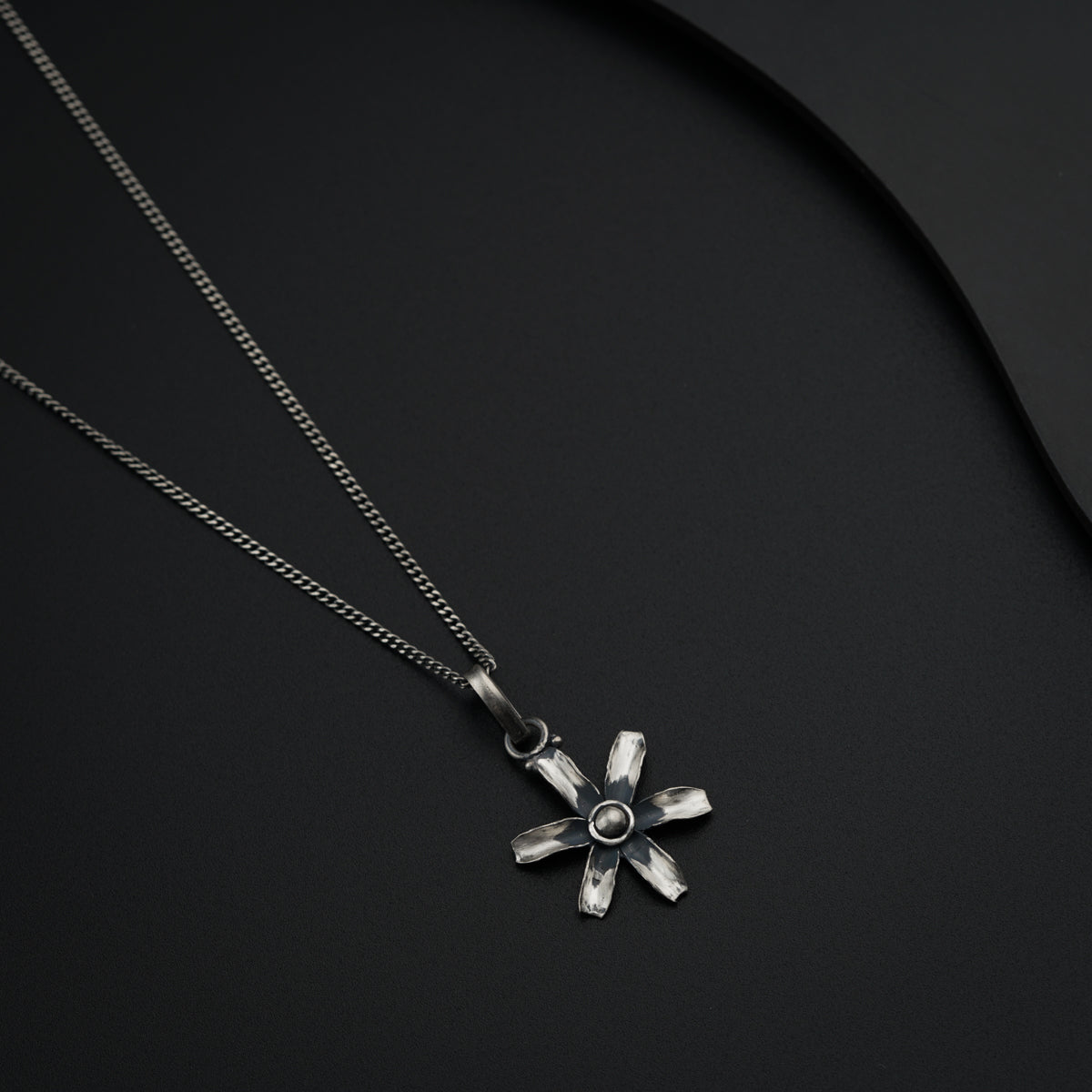 a silver necklace with a flower design on a black background