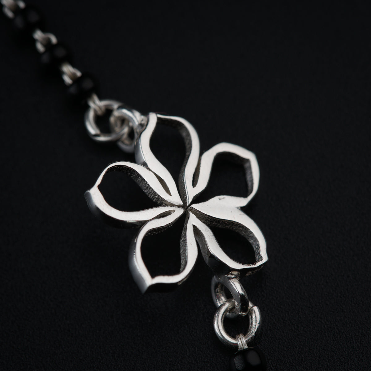 a silver flower on a chain on a black background
