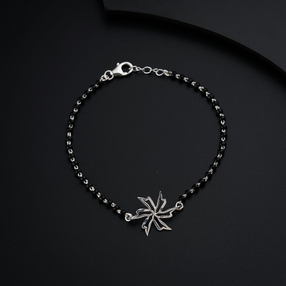 a black beaded bracelet with a silver leaf charm