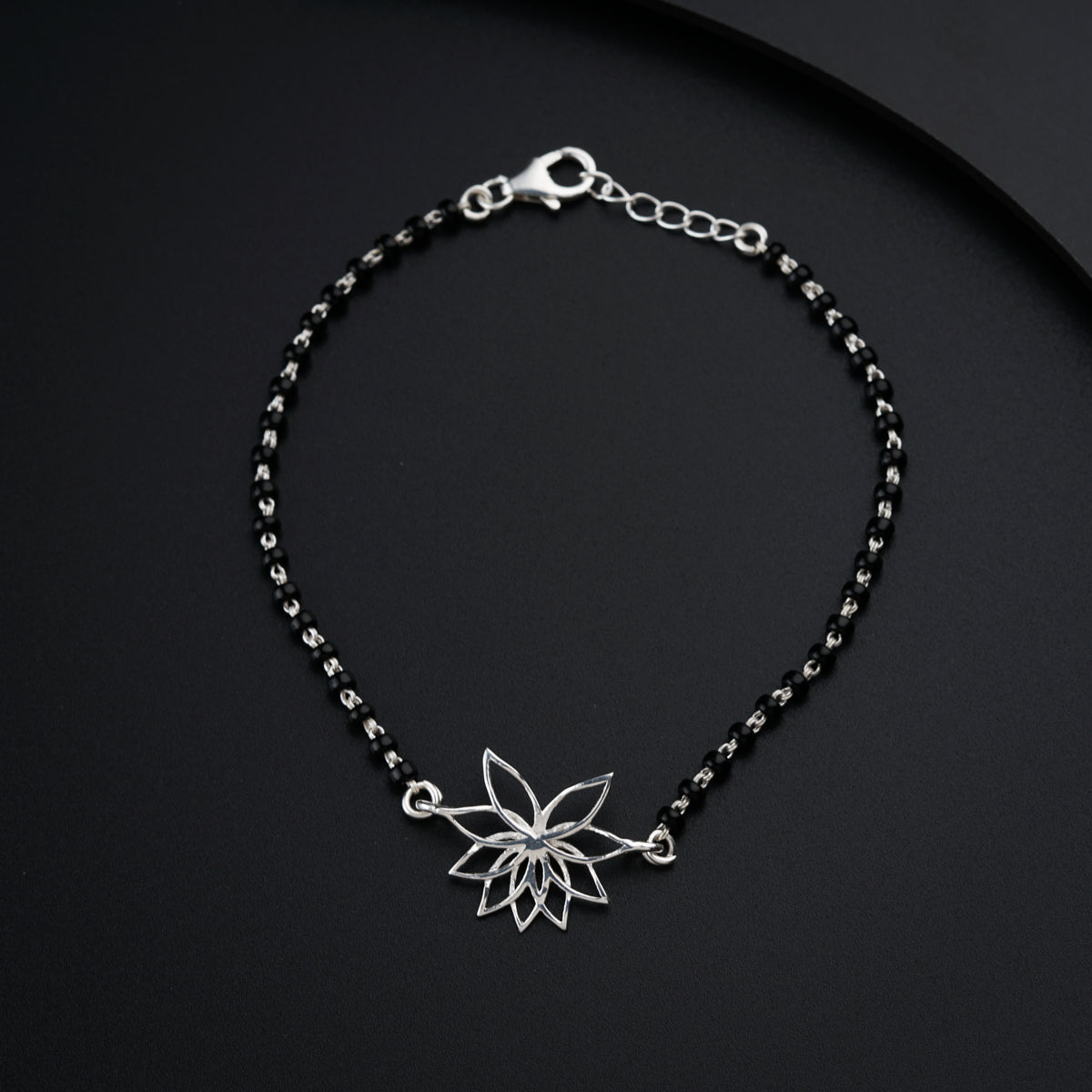 a black beaded bracelet with a silver flower charm