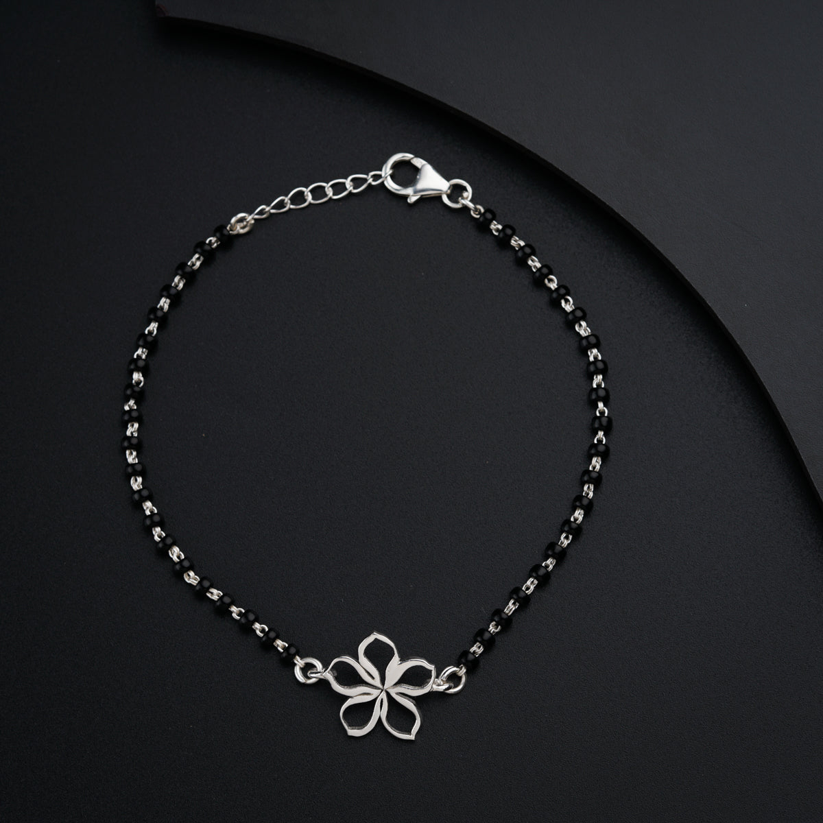 a black beaded bracelet with a silver flower charm