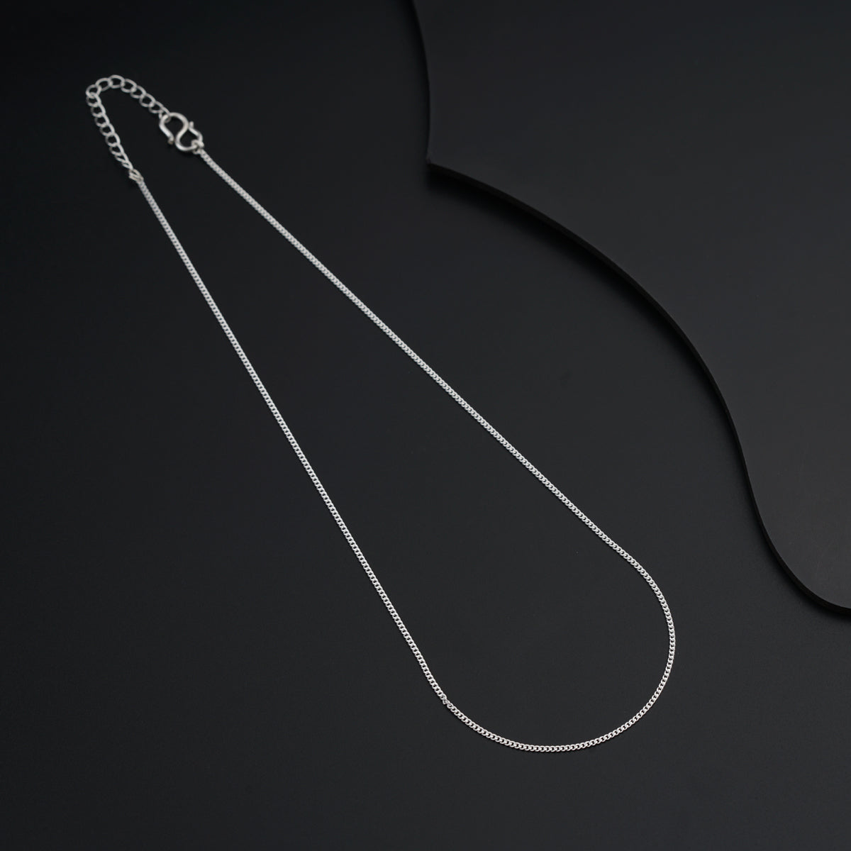 a silver necklace with a chain on a black background