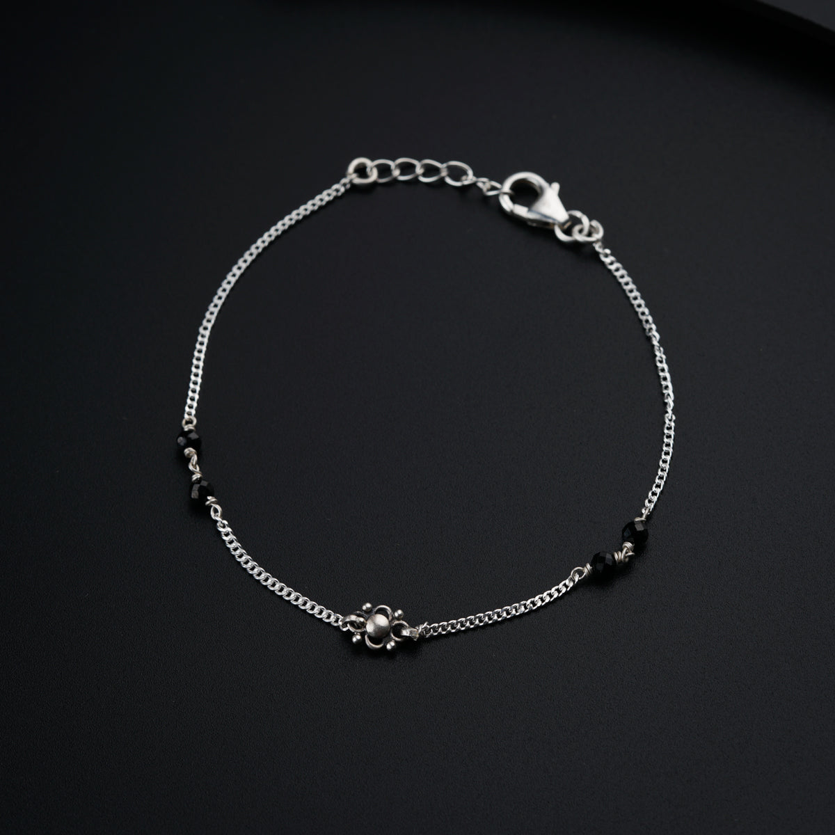 a silver bracelet with black beads on a black surface