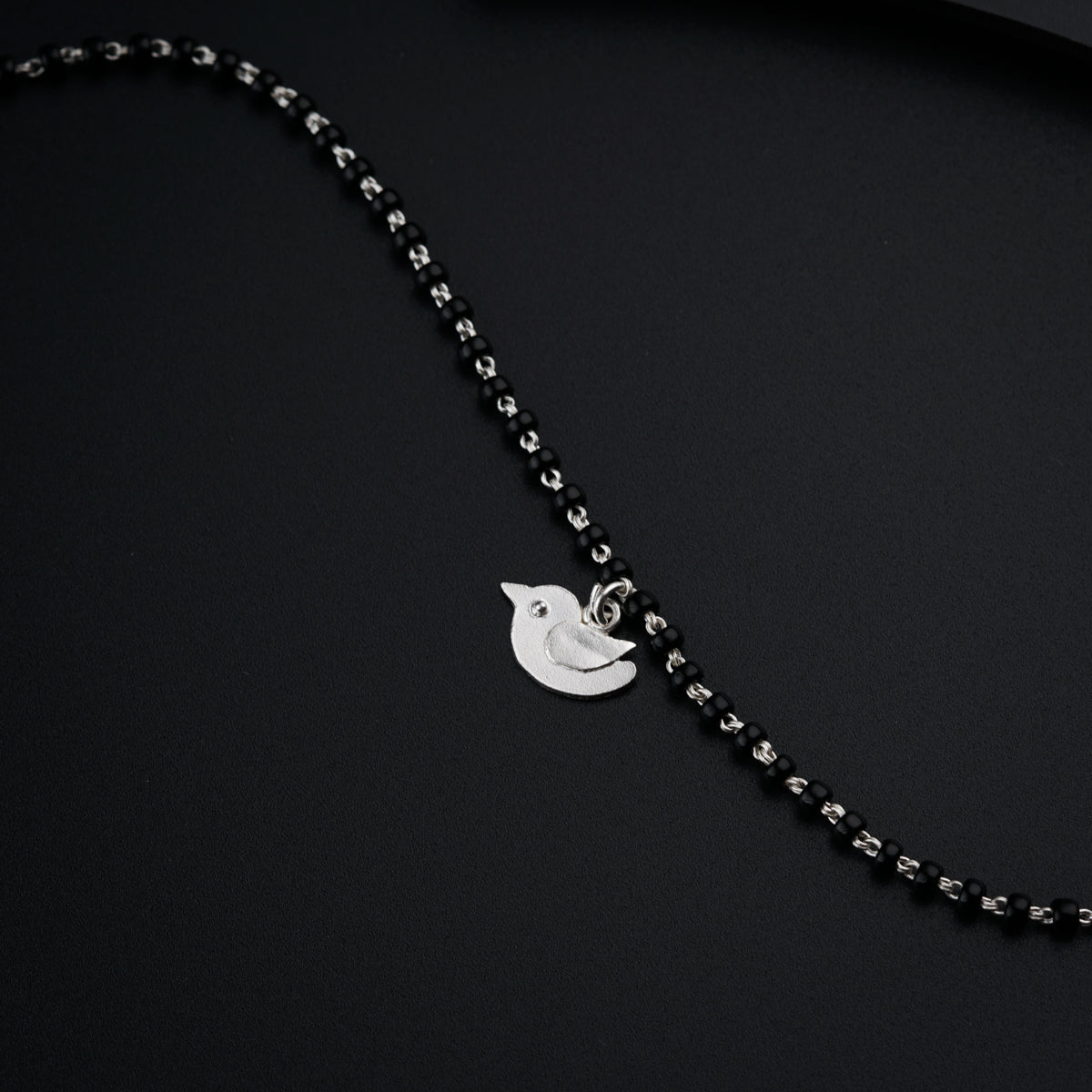 a necklace with a bird on it on a black surface