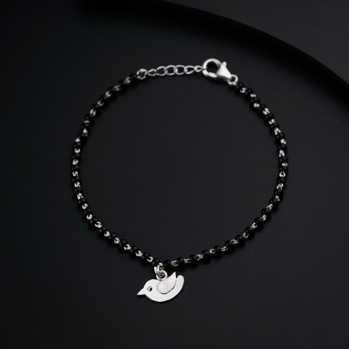 a black beaded bracelet with a silver bird charm