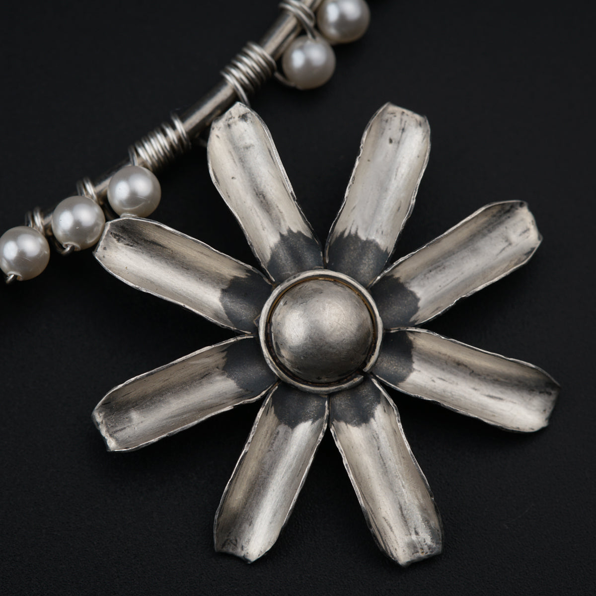 a silver necklace with pearls on a black background