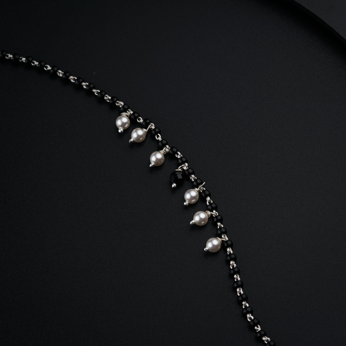 a black and silver necklace with pearls on a black background