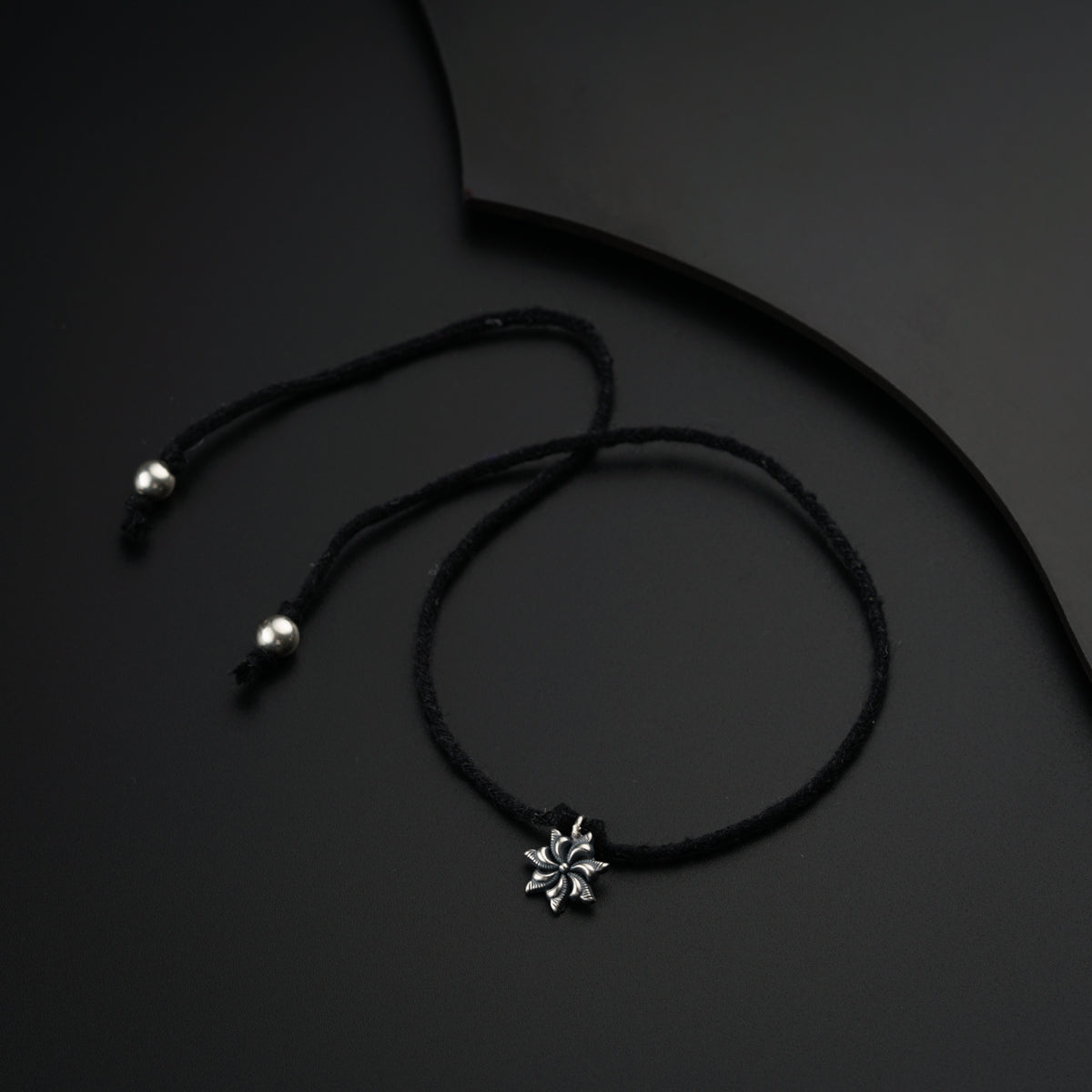a black necklace with a flower on a black background