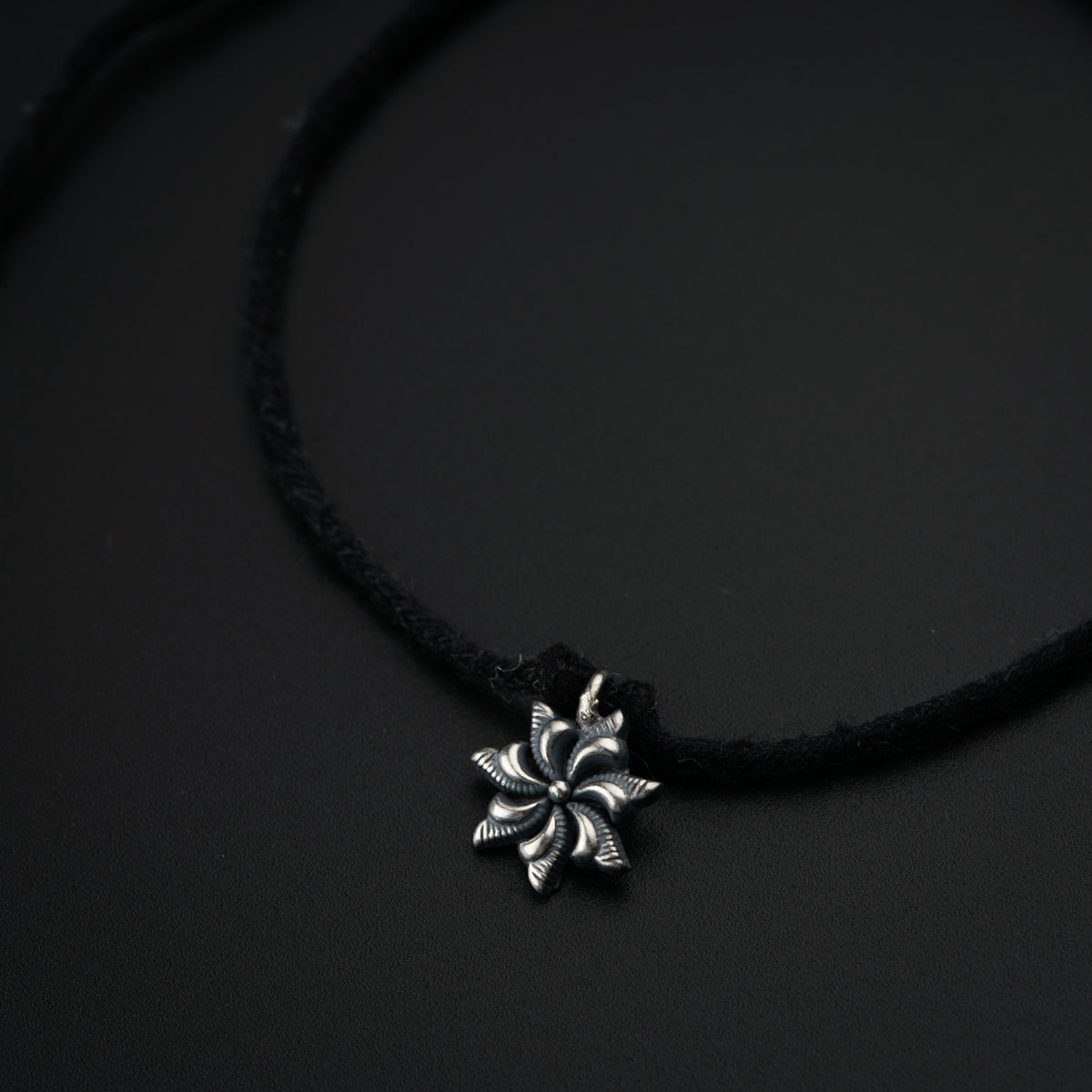 a black cord necklace with a silver flower pendant