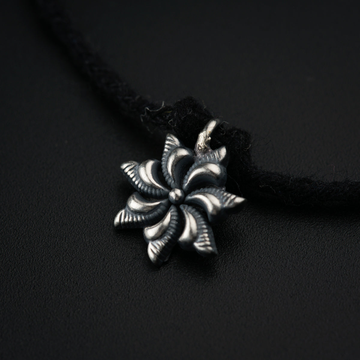 a silver flower pendant on a black cord