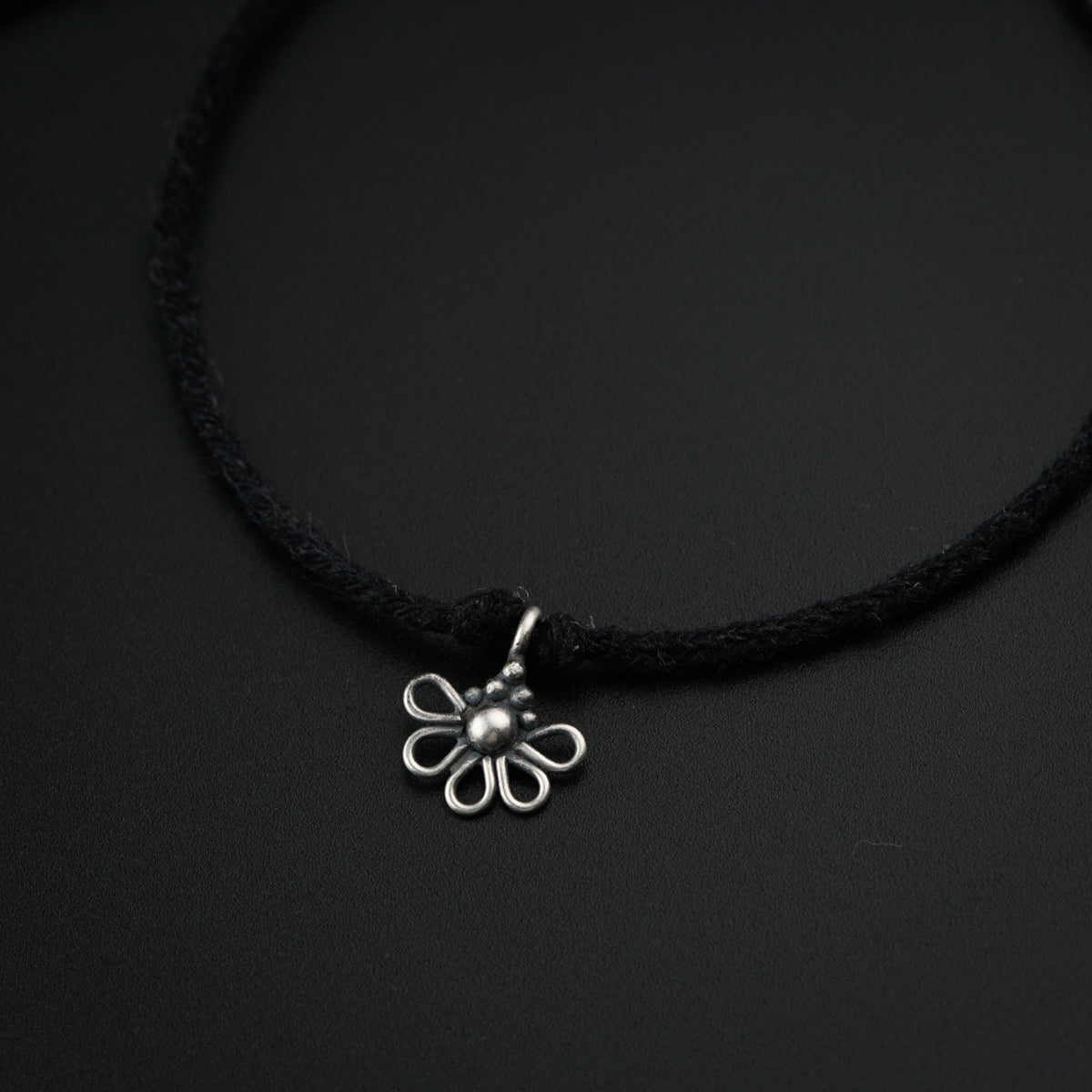 a black cord necklace with a silver flower charm