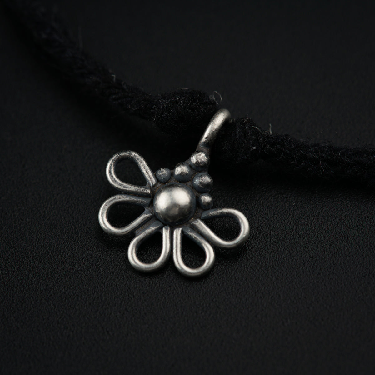 a silver pendant with a flower on a black background