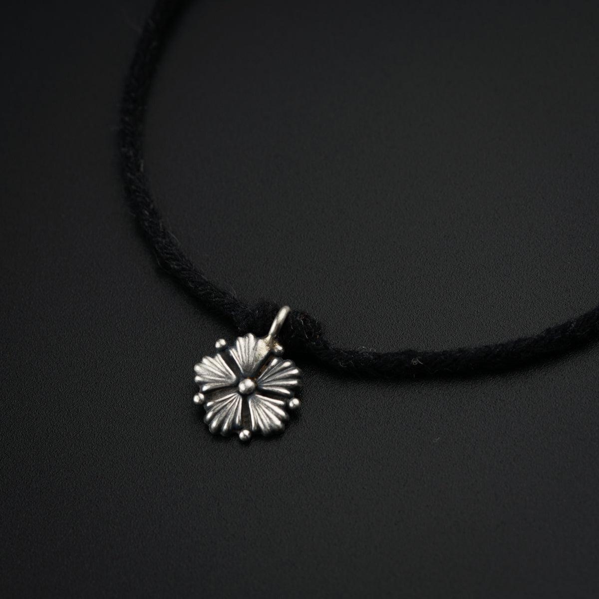 a black cord necklace with a silver flower charm