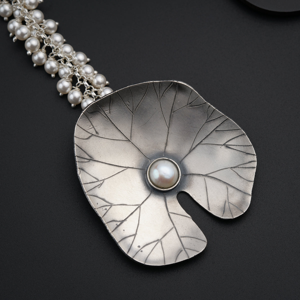 a silver necklace with a leaf and a pearl