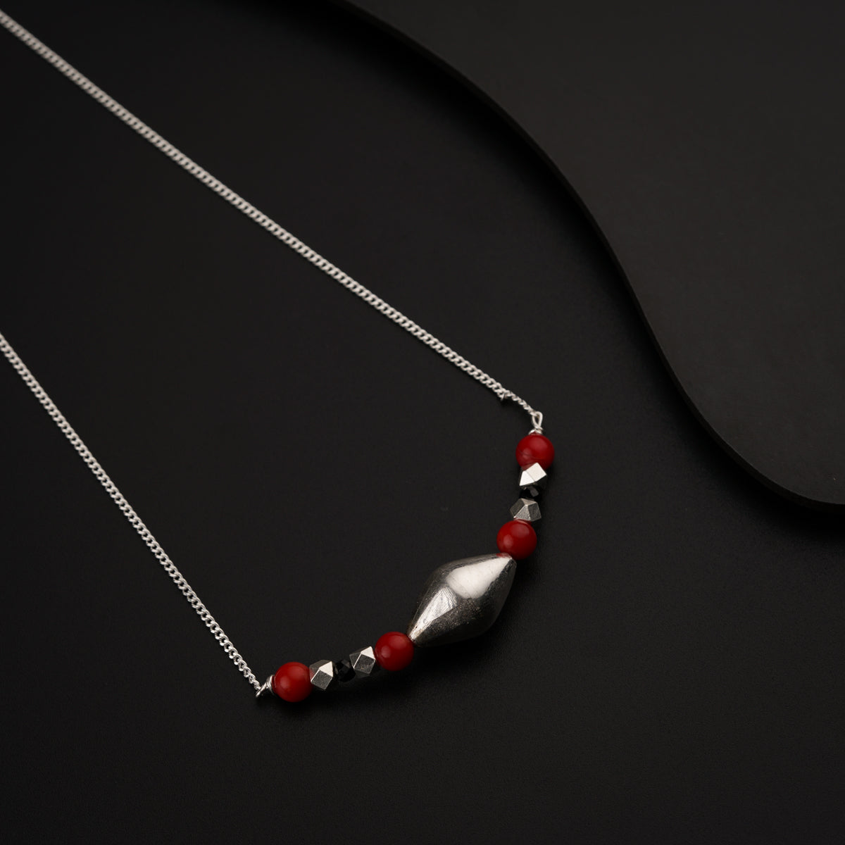 a silver necklace with red beads on a black surface