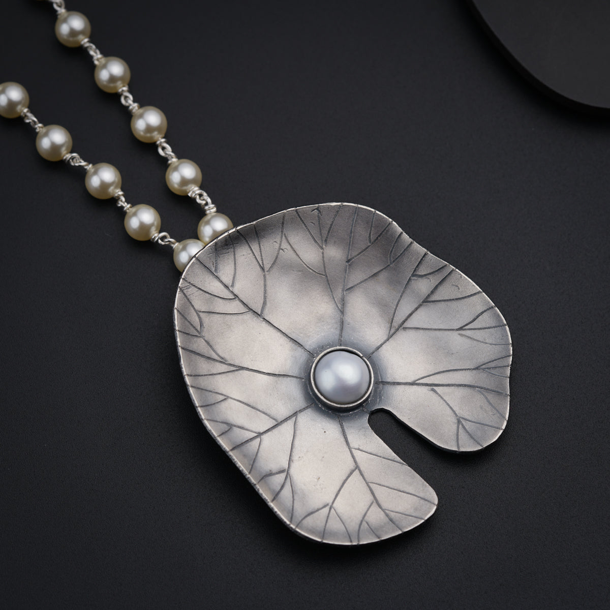 a necklace with a leaf and a pearl
