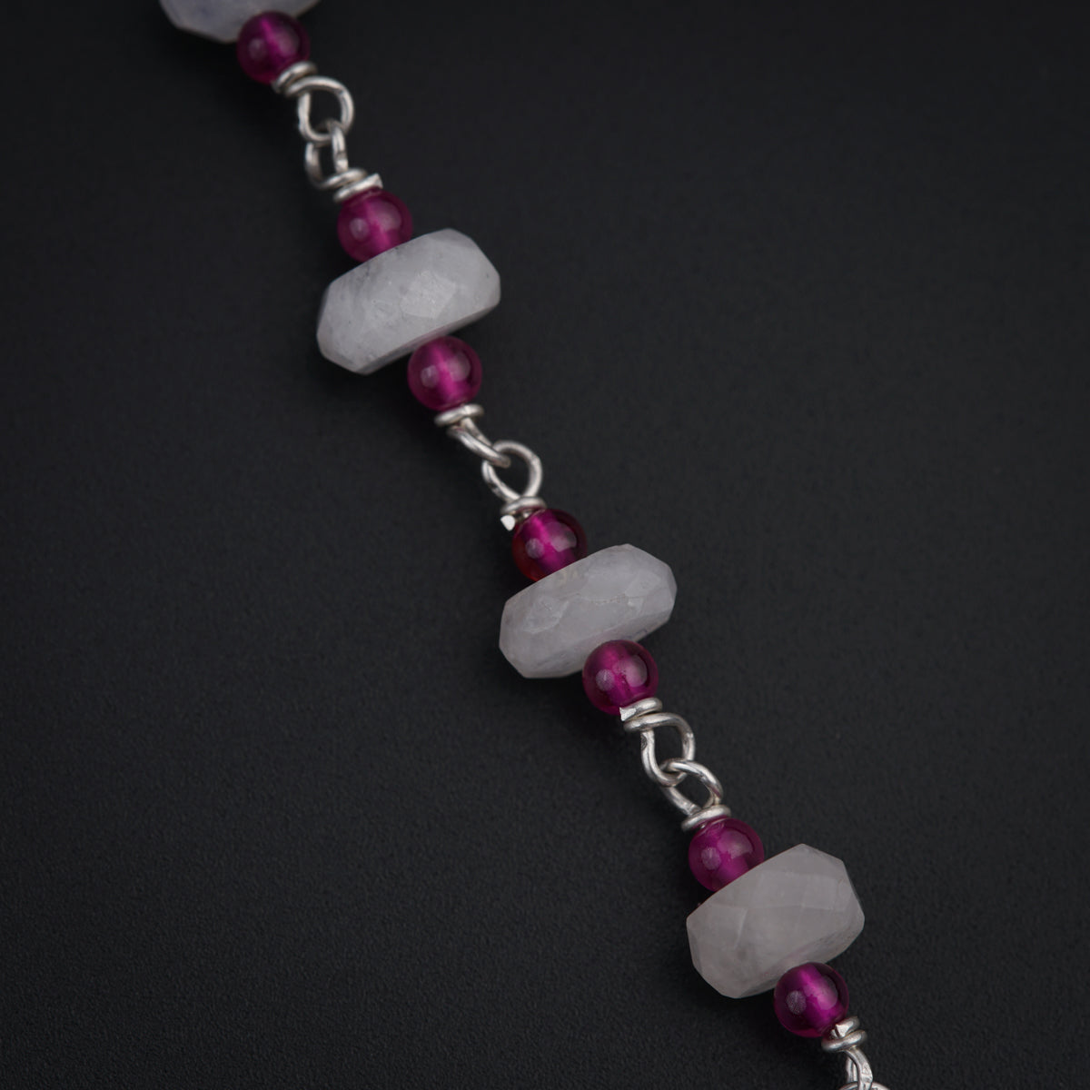 a bracelet with beads and a chain on a black surface