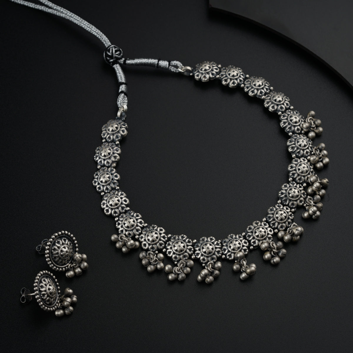 a silver necklace and matching earrings on a black surface