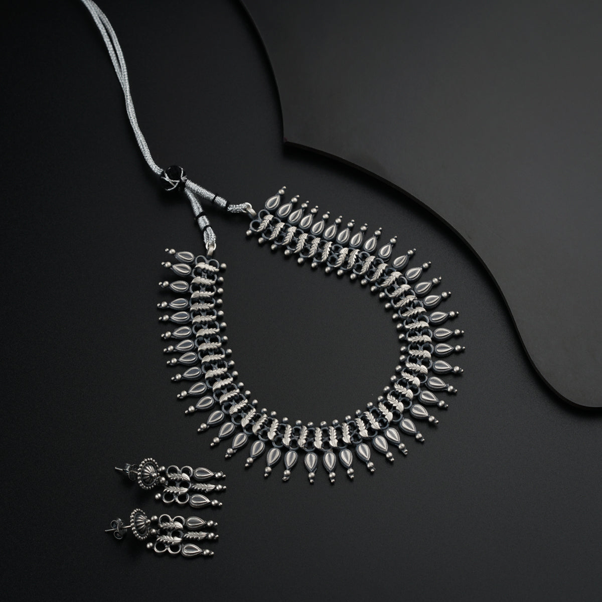 a silver necklace and matching earrings on a black surface