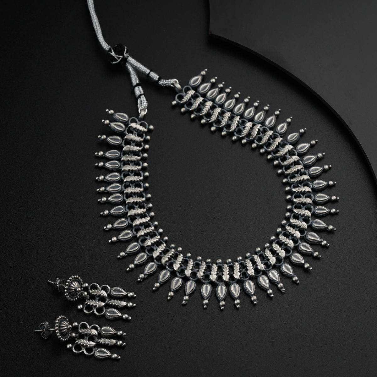 a silver necklace and matching earrings on a black surface