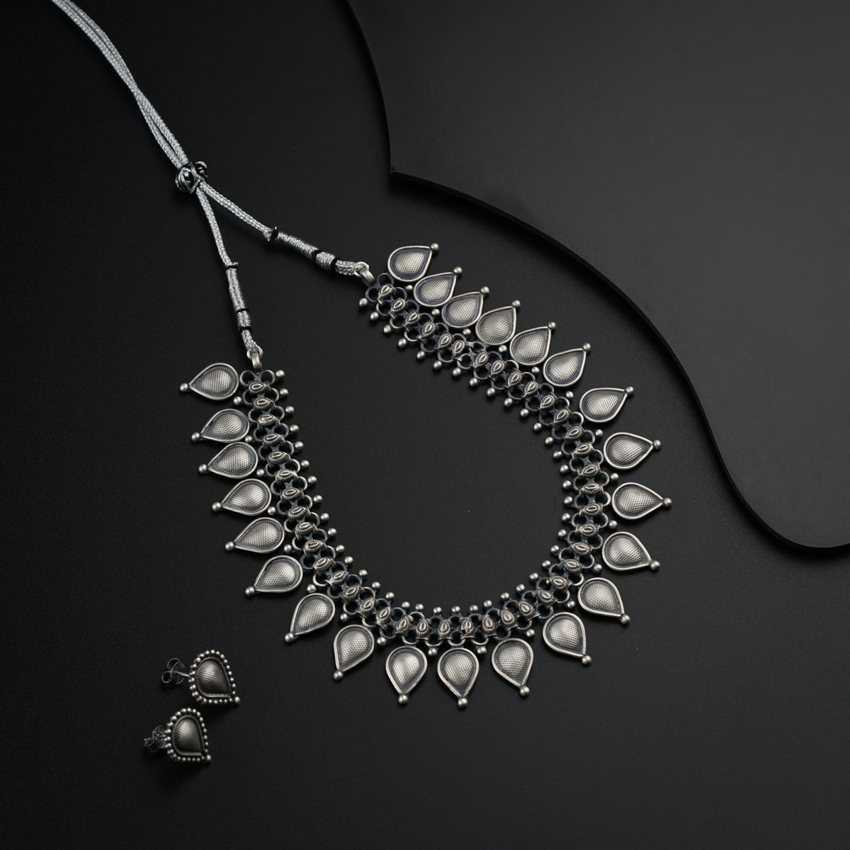a silver necklace and matching earrings on a black surface