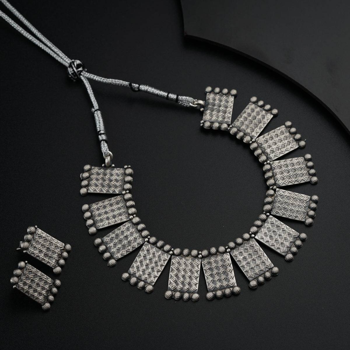 a silver necklace and matching earrings on a black surface