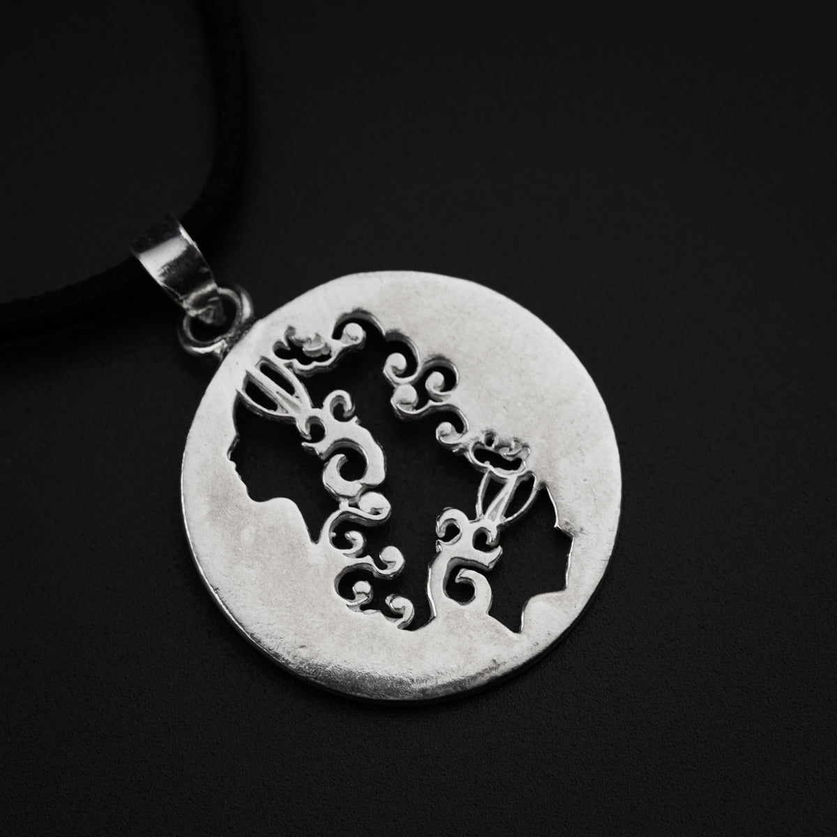 a silver pendant with a black cord on a black background