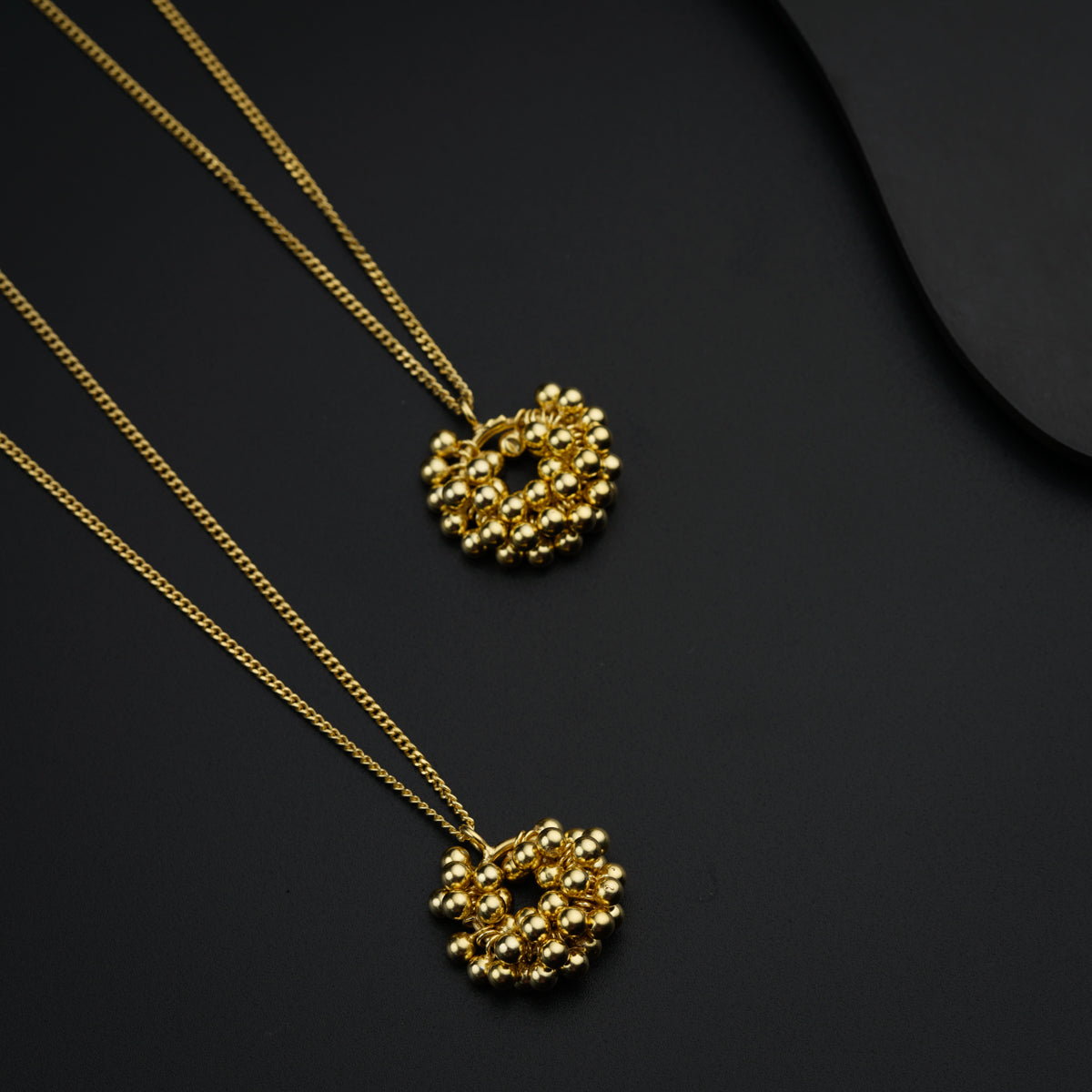 two gold necklaces on a black surface