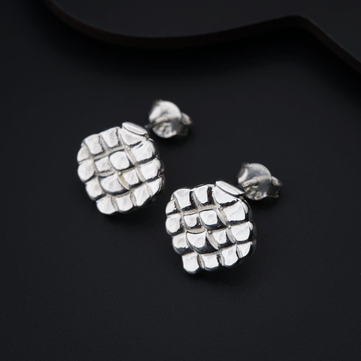 a pair of silver earrings sitting on top of a black surface