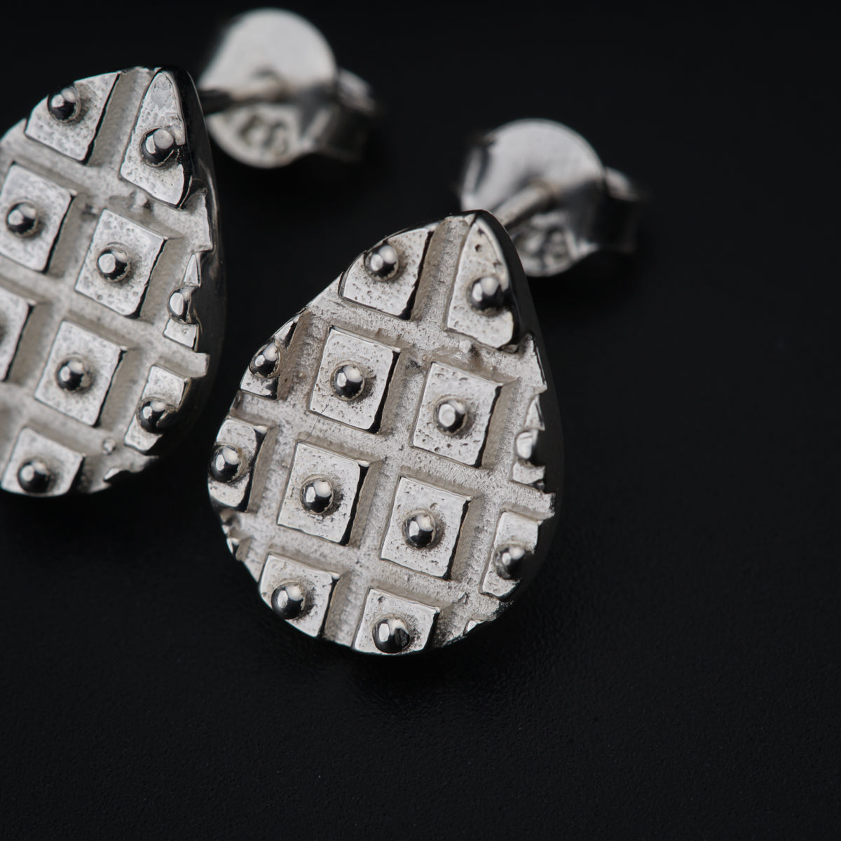 a pair of silver earrings sitting on top of a black surface