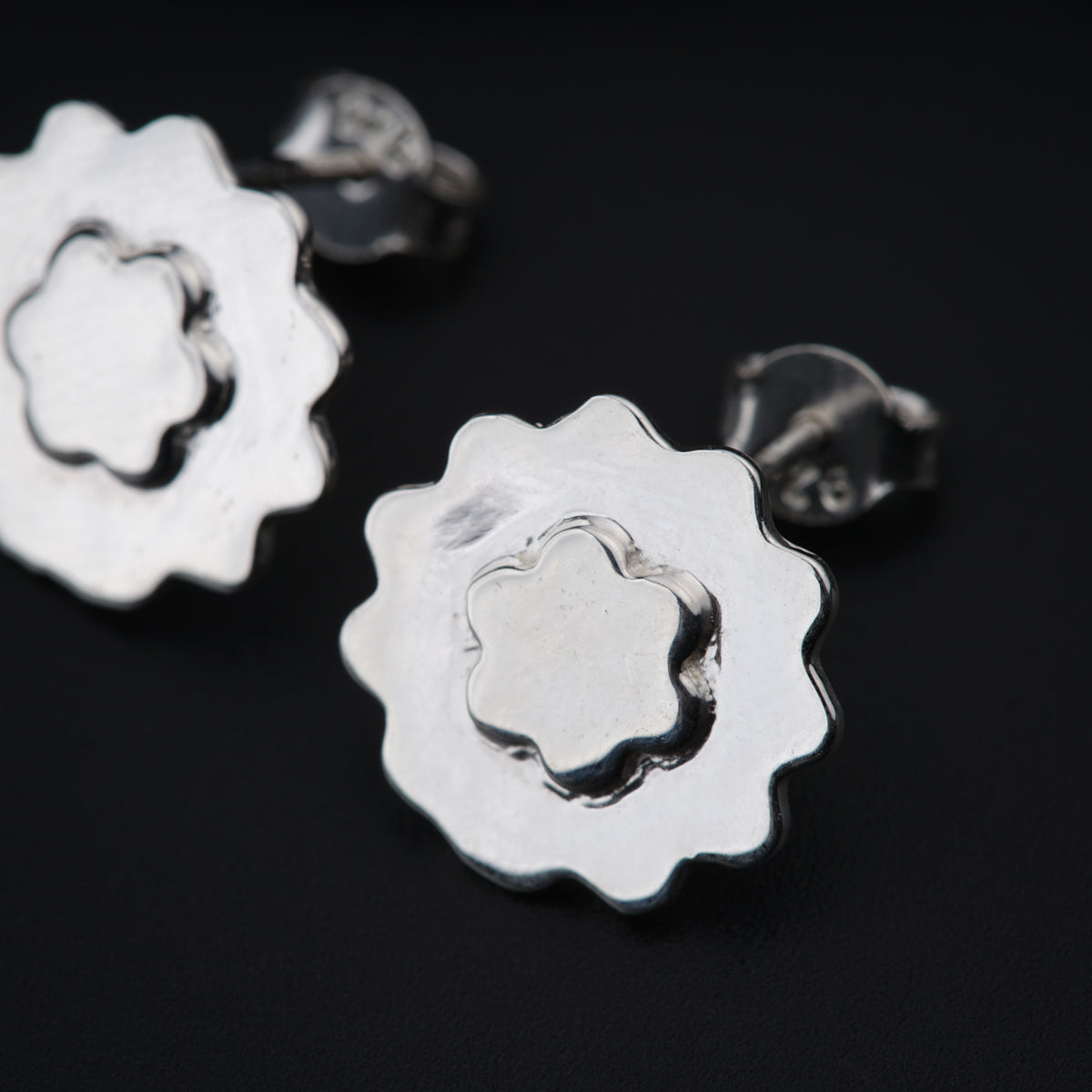 a pair of silver flower earrings on a black background