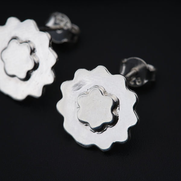 a pair of silver flower earrings on a black background