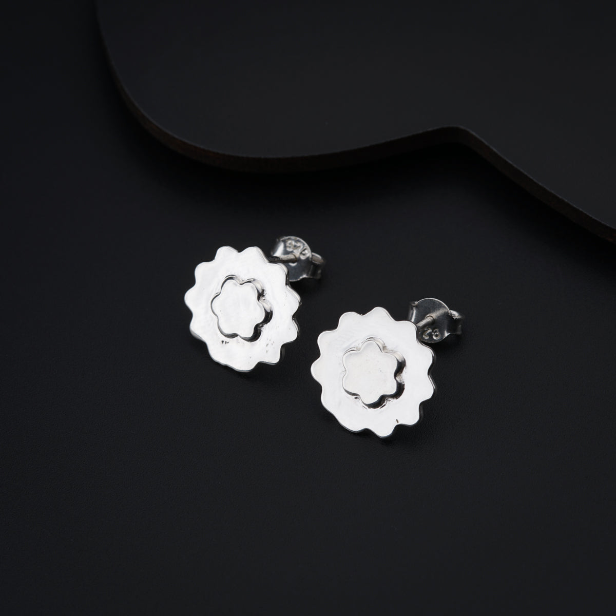 a pair of silver flower earrings on a black background