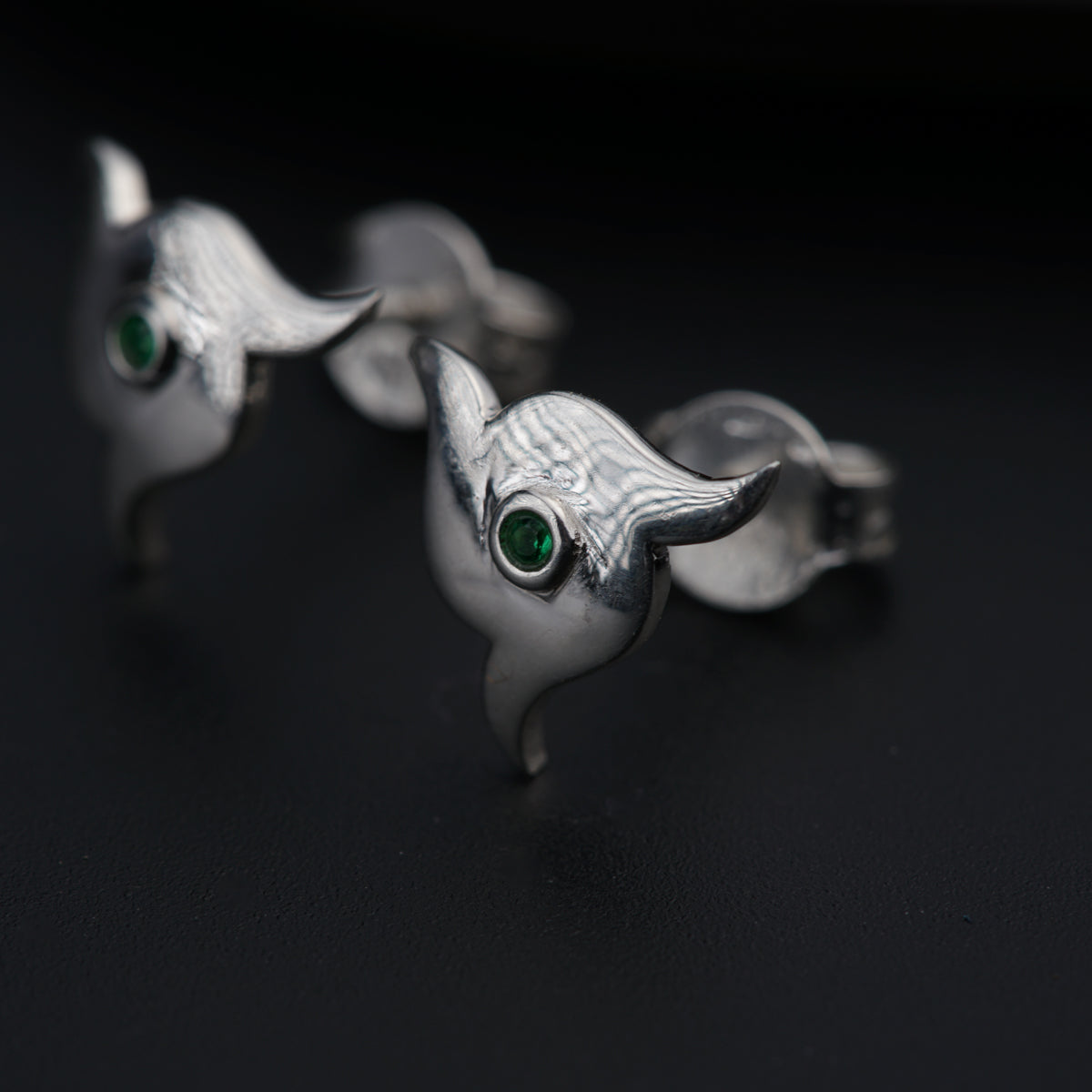 a pair of silver earrings with green eyes
