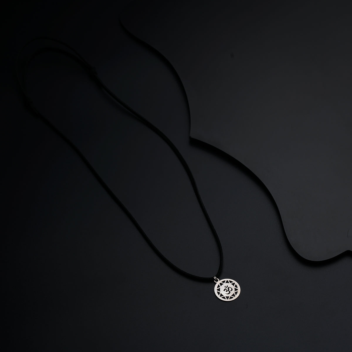 a black necklace with a silver pendant on a black background