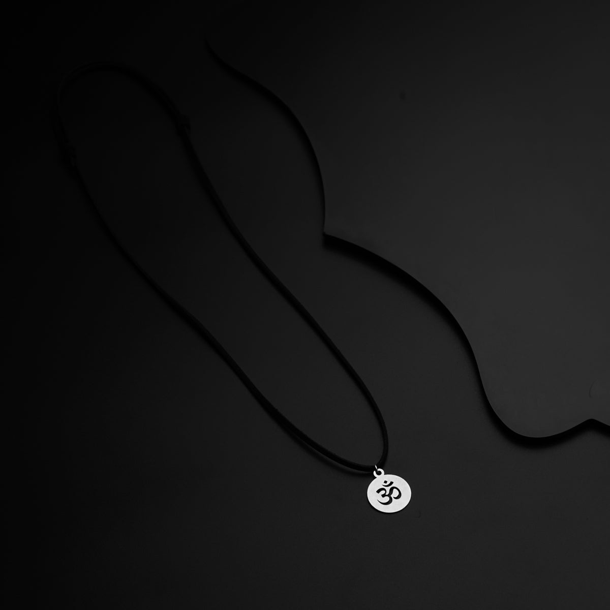 a black necklace with a silver pendant on a black background