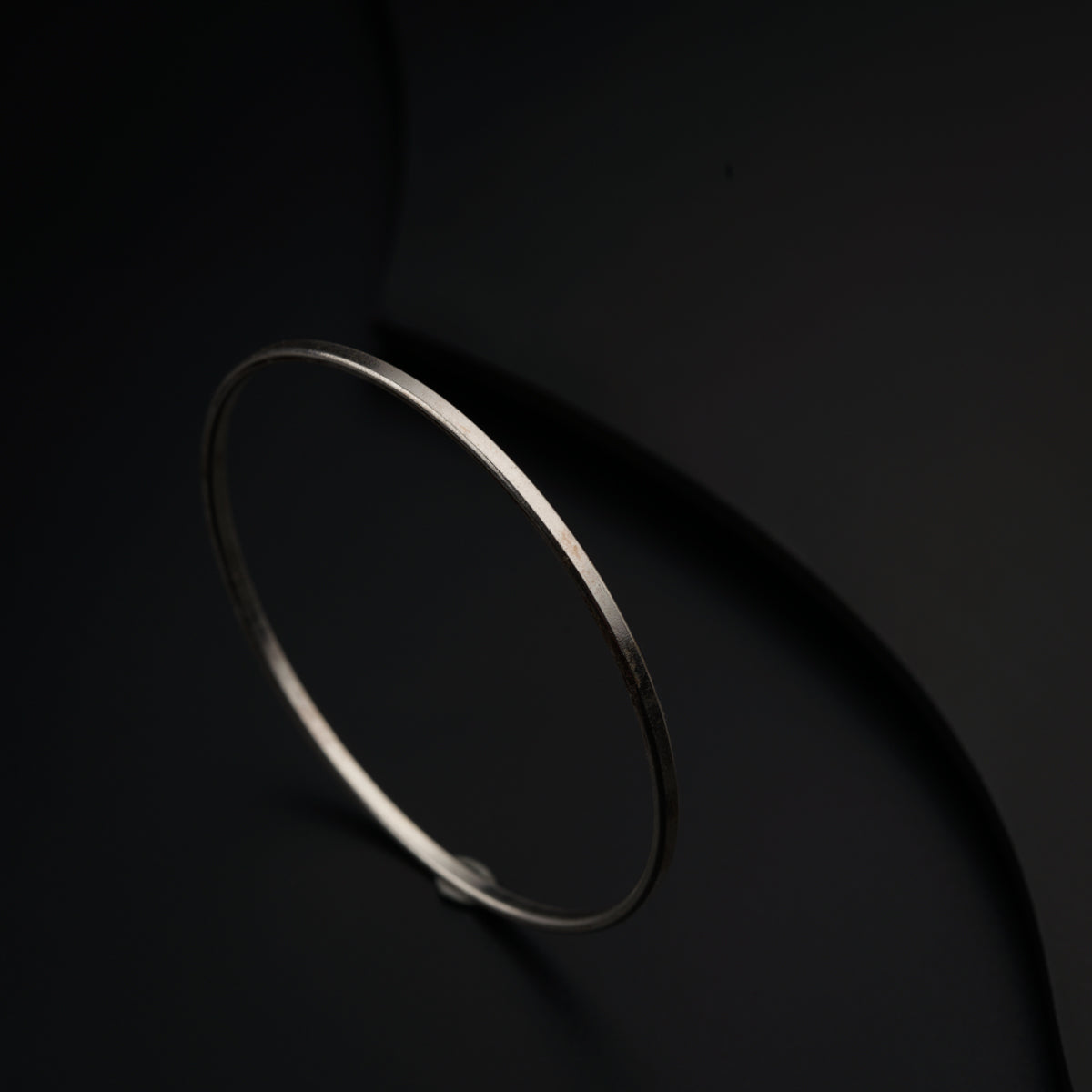 a thin silver bracelet on a black surface